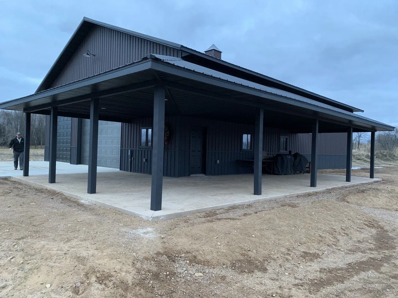 Dark Grey Metal Custom Home with Wraparound Porch An exterior shot of a large custom dark grey metal home, showcasing its deep wraparound porch supported by multiple pillars.